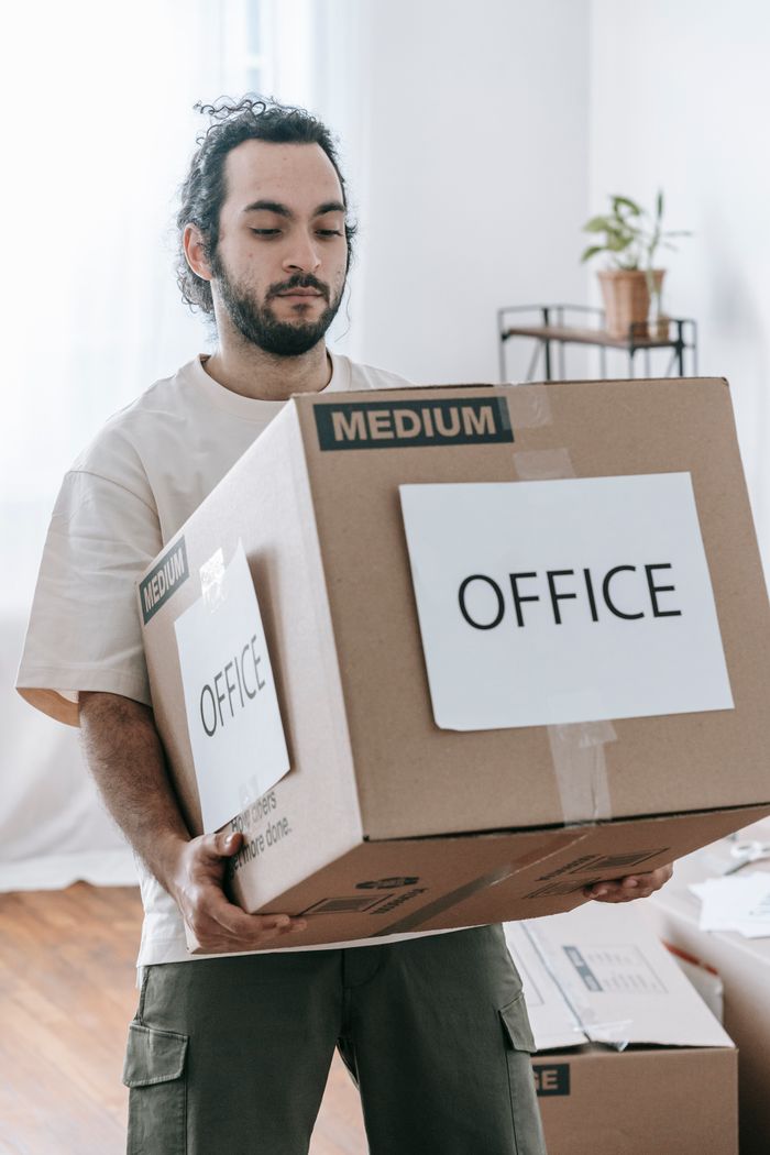 Man moving box labeled Office indoors during relocation or packing.