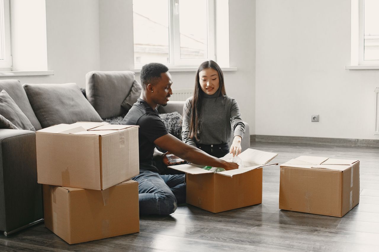 Happy couple unpacking moving boxes in their new apartment living room.